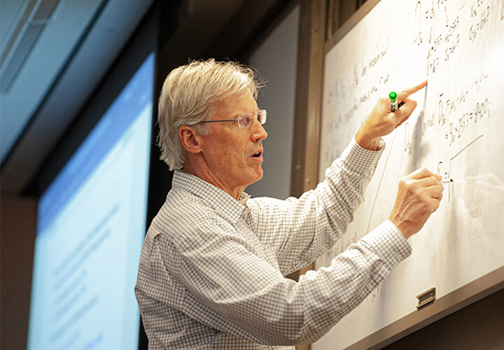 Professor writes on white board while teaching a class