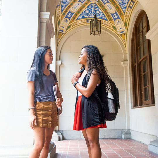 Two students talk under archway on University of Texas campus