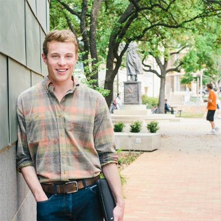 Student leans against an outside wall on University of Texas campus