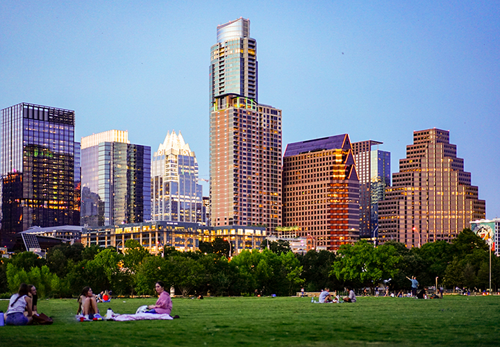 People sitting on grassy field with Austin skyline in background