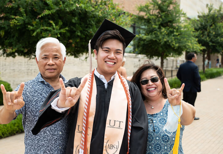 Smiling graduate gives hook em horns and poses with family