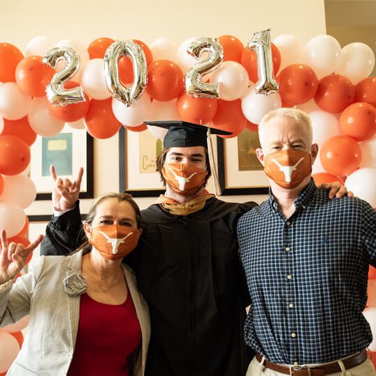 Masked graduate and family members under balloon arch