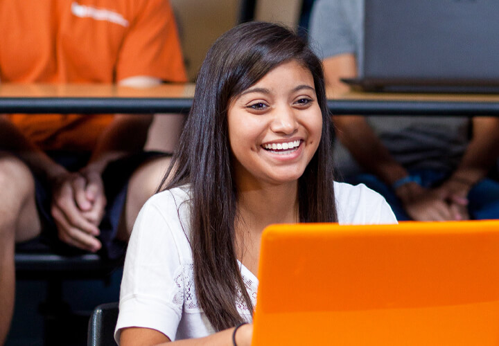 Smiling female student sitting in a classroom with a orange laptop