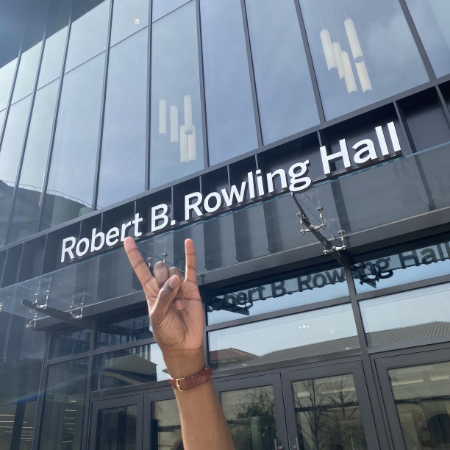 hand holding up the hook em hand sign with Rowling Hall in the background