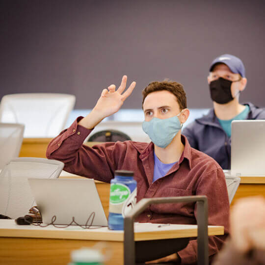 Masked student raises hand in class