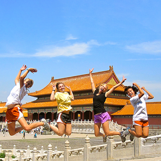 Four students jumping in front of a pagoda in Asia