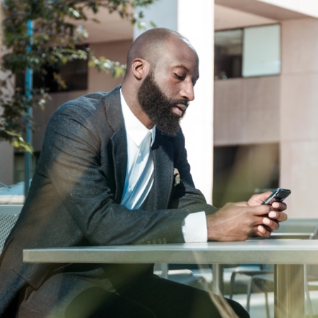 Man sitting at a table looking at cell phone while wearing a suit.